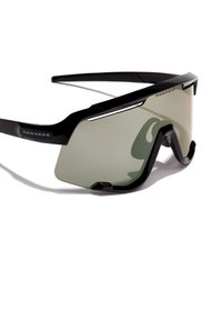Schwarze Sonnenbrille mit großen, kantigen Rahmen und grünen Gläsern. Sie zeichnet sich durch ein elegantes Design und metallische Akzente aus und ist mit "HAWKERS" beschriftet.