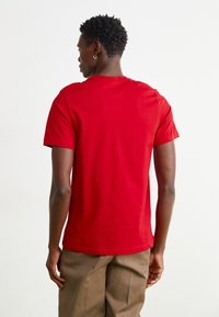 Rød bomulds t-shirt med rund hals og korte ærmer, glat tekstur og tætsiddende pasform, set bagfra.