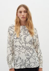 Blusa in tessuto crema con motivi floreali disegnati a linee nere, maniche lunghe con polsini arricciati e scollo rotondo con patta.