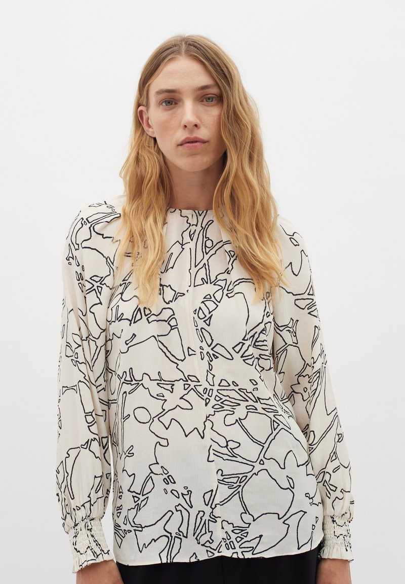 Blusa in tessuto crema con motivi floreali disegnati a linee nere, maniche lunghe con polsini arricciati e scollo rotondo con patta.
