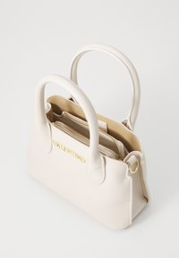 Bolso de mano de cuero beige que cuenta con dos asas superiores, un logo dorado y compartimentos interiores con cremallera para una mejor organización. Textura suave.