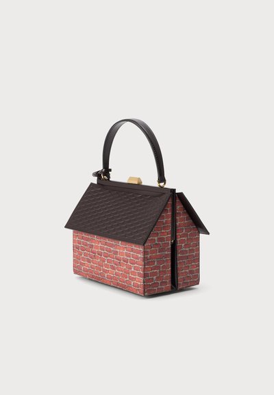 Sac à main en forme de petite maison avec des murs en briques rouges, un toit sombre texturé, une poignée noire et un fermoir doré sur le dessus.
