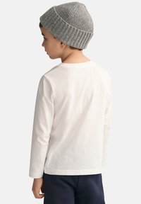 Hvit langermet skjorte med rund hals, sammen med en grå ribbet lue. Skjorten har en glatt tekstur og et enkelt design.