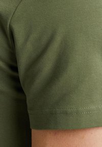 T-shirt a maniche corte verde oliva realizzato in morbido cotone, con una texture liscia e orlo pulito con dettagli di cucitura minimi.