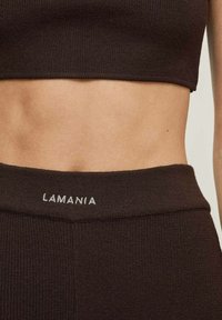 Ruda suglebta trumpa palaidinė ir atitinkantys aukštai juosmeniški Legginai, su subtiliu „LAMANIA“ logotipu, išsiuvinėtu šviesiame toną ant juosmens.