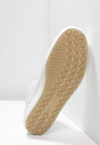 Weißer Sneaker mit einem glatten Leder-Obermaterial, Gummisohle mit einem strukturierten, gepunkteten Griffmuster in Beige. Seitenansicht von unten.