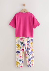 Rózsaszín rövid ujjú pamut póló, fehér nadrággal, amely színes pillangó és masni mintával díszített. Könnyű és laza kialakítás.