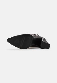 Zapato de tacón negro con parte superior de cuero texturizado que presenta un patrón de cocodrilo. Tacón cuadrado y suela de goma con marca en la parte inferior.