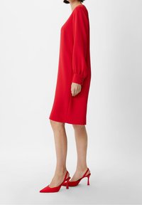 Vestido rojo de manga larga, de corte suelto y con mangas de globo. Longitud por debajo de la rodilla, textura suave, adornado con detalles de botones.