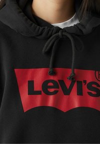 Sweat à capuche noir avec un logo Levi's rouge et un graphisme, doté de cordons de serrage réglables et d'une texture de tissu douce.