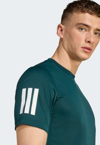 Dark green athletic t-shirt with short sleeves, featuring a smooth texture and three white stripes on the left shoulder.