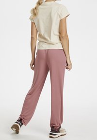 Béžové bavlněné tričko s ohrnutými rukávy v kombinaci s volnými růžovými strečovými kalhotami. Mezi pozoruhodné detaily patří manžety u kotníků a tenisky.