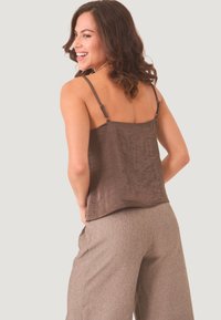 Top de satén marrón sin mangas con tirantes ajustables, que presenta un corte holgado y una textura sutil. Combinado con pantalones de pierna ancha, texturizados, en gris claro.