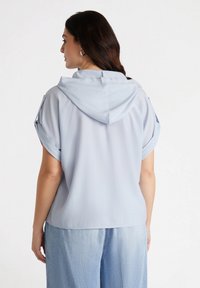 Top corto a maniche corte di colore azzurro chiaro con cappuccio, caratterizzato da maniche arrotolate e una vestibilità comoda. Texture liscia, design casual adatto per sovrapposizioni.