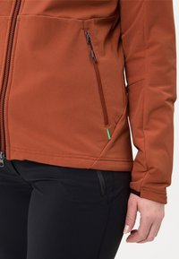 Roodbruine softshelljas met een gestructureerd oppervlak, voorzien van een voorzak met rits en contrasterende donkere stof bij de manchetten.