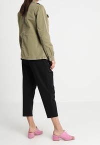 Oliivinvihreä työtyylinen takki, mustat lyhyet housut ja vaaleanpunaiset avoimet mules-kengät. Painotus rentoon, mukavaan istuvuuteen ja toimivaan muotoiluun.