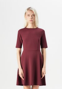 Rochie bordo cu un corset ajustat și fustă evazată. Prezintă mâneci scurte, decolteu rotund și un material fin, texturat.