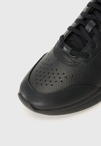 Zapatillas negras con un upper de cuero texturizado, detalles perforados y una suela de goma lisa. Presentan cordones negros y un diseño de perfil bajo.