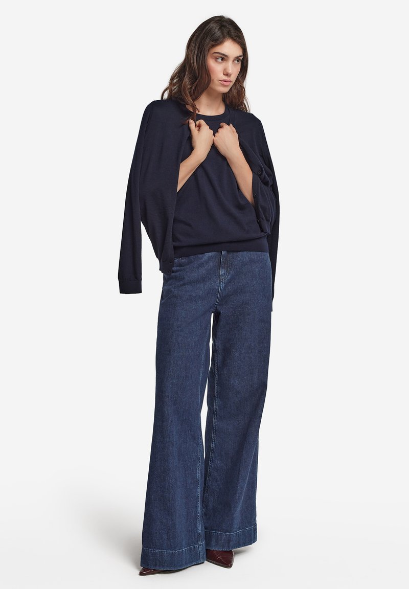 Marinblå långärmad topp med sänkta axlar, i kombination med vida mörk denimjeans med råa kanter och en avslappnad passform.