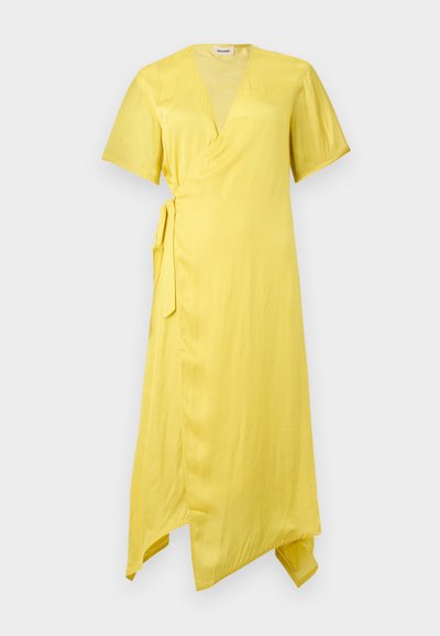 Κίτρινο φόρεμα τύπου wrap με κοντά μανίκια, V-λαιμόκοψη, δέσιμο στο πλάι και ασύμμετρο τελείωμα σε απλό γκρι φόντο.