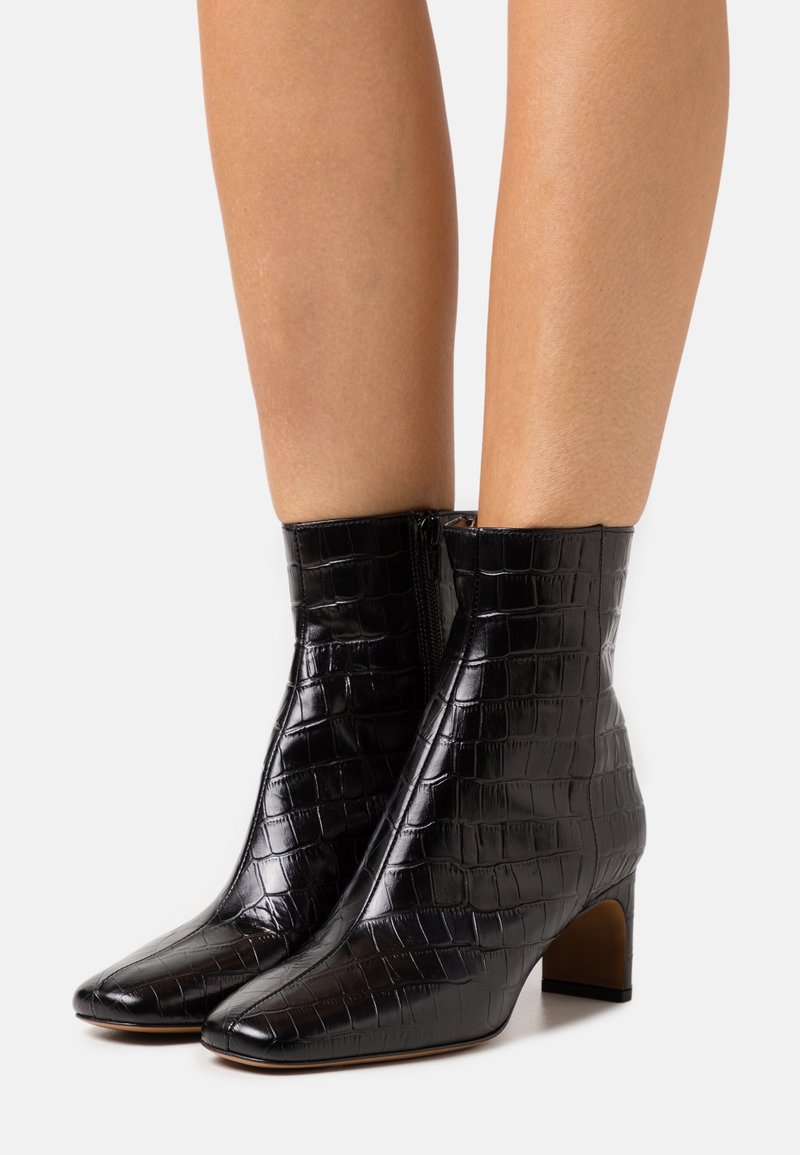Botas negras hasta el tobillo hechas de cuero con estampado de cocodrilo, con puntera afilada y tacón cuadrado. Detalle de cremallera en el lado.