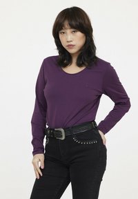 T-shirt violet à manches longues avec un col rond et un détail de logo subtil, associé à un jean noir taille haute avec des accents cloutés.