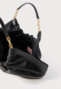 Zwarte leren handtas met gouden ketting en leren handvatten, open bovenkant die het binnenvak met rits en het merkembleem toont.