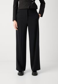 Black wide-leg trousers with a smooth texture, featuring side pockets and subtle perforated detailing along the sides.