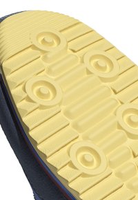 Shoe sole featuring a textured yellow rubber surface with raised circular and ridged patterns, bordered by a dark material on the edge.