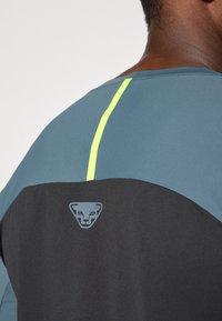 Maglietta sportiva da uomo con una parte superiore blu scuro, parte inferiore nera e una striscia verticale giallo neon. Include un logo vicino al colletto.