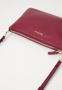 Burgundy leather clutch with textured surface, gold zipper, and strap. Features embossed logo and gold hardware accents.