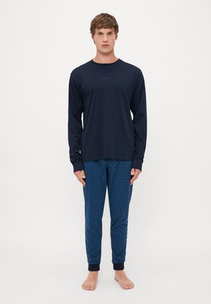 Marineblaues Langarmoberteil mit subtiler Markenkennzeichnung, kombiniert mit gemusterten blauen Hosen mit geometrischem Design und gerippten Bündchen.