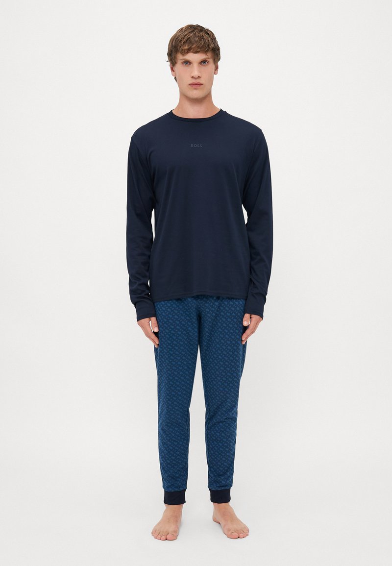 Camisa de manga longa azul-marinho com uma marcação discreta, combinada com calças azuis estampadas com um design geométrico e punhos canelados.