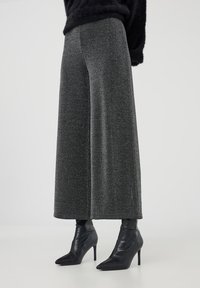 Pantaloni a gamba larga in tessuto grigio testurizzato, con vita alta e tasche laterali, abbinati a stivali neri con tacco a punta.