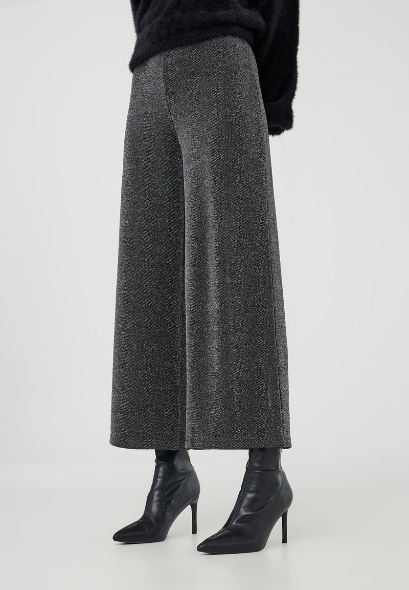 Pantaloni a gamba larga in tessuto grigio testurizzato, con vita alta e tasche laterali, abbinati a stivali neri con tacco a punta.