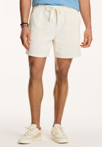 Pantaloni scurți din corduroy de culoare crem, cu talie elastică și șnur. Purtați cu adidași crem, evidențiind un aspect casual.