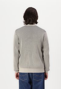 Grå tekstureret cardigan med ribbet design, rund halsudskæring og beige kant ved ærmerne og nederste kant, parret med blå denimjeans.