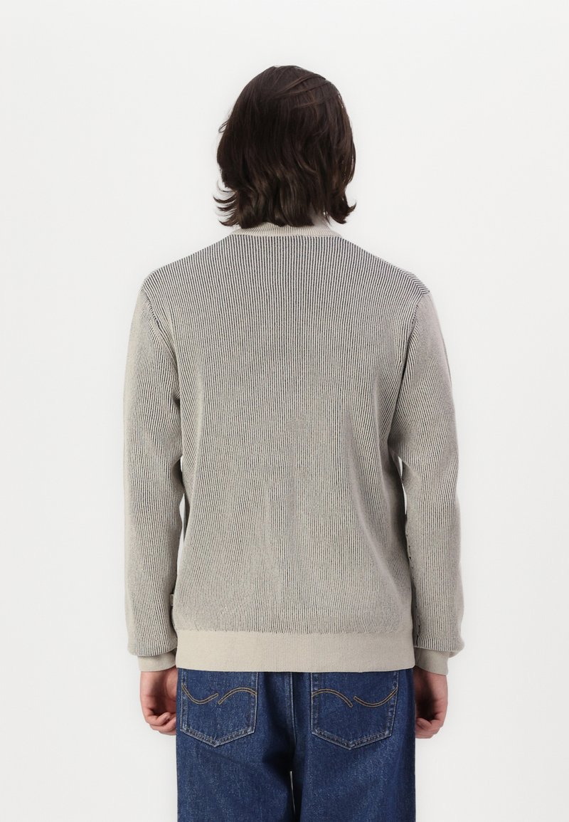 Cardigan grigio con texture e design a coste, scollatura arrotondata e rifiniture beige ai polsini e all'orlo, abbinato a jeans in denim blu.