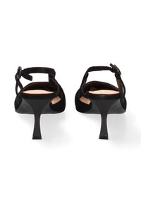 Zwarte suède slingback kitten heels met verstelbare enkelbandjes en smalle tapse hakken, gezien van achteren op een witte achtergrond.