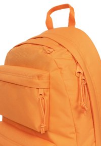Oranžový látkový batoh s kulatým tvarem, přední kapsou se zipem a odpovídajícími šňůrkami pro bezpečné zavření.
