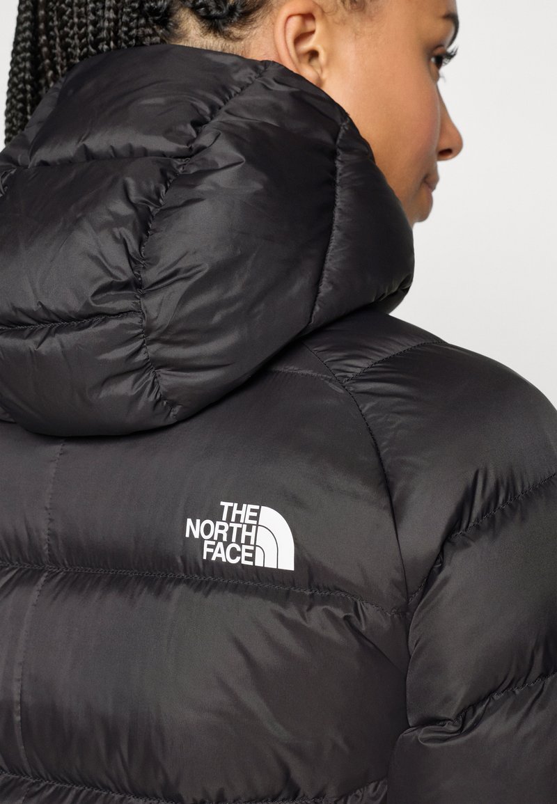 Sort puffers jacket med høj krave, prydet med et hvidt logo på venstre side. Glat, skinnende ydre med kviltede syninger.