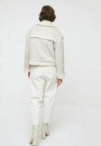 Chaqueta corta de piel de oveja blanca forrada, con mangas amplias, textura suave y color claro, combinada con pantalones blancos de talle alto y botas de tobillo.