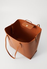 Brun lær totebag med en strukturert overflate, åpen topp, to håndtak og magnetlås inni. Minimalistisk design, ingen synlig maskinvare.