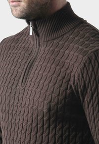 Brązowy sweter z dzianiny z teksturowanym, kablowym wzorem, wysokim prążkowanym kołnierzem i pół zamkiem błyskawicznym przy szyi.