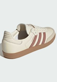 Off-white Adidas Samba-sneaker med brune lærstriper, gummisåle og teksten "SAMBA" på siden, vist fra baksidevinkel.