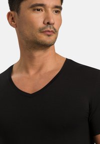 Czarny bawełniany T-shirt o dekolcie w serek z krótkim rękawem, gładka tekstura i dopasowany krój. Dekolt ozdobiony subtelną, wykończoną lamówką.