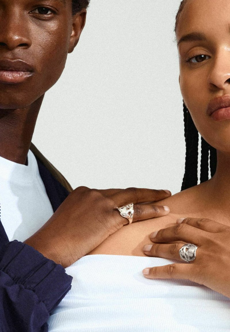 Due individui con le mani che si toccano. Uno indossa un anello in argento con texture, l'altro ha un anello scultoreo in oro. Entrambi hanno tonalità di pelle naturali.