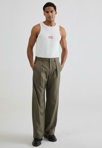 Top alb cu text roșu, combinat cu pantaloni largi de culoare verde oliv. Pantalonii au închidere cu nasture și buzunare laterale. Încălțăminte neagră.