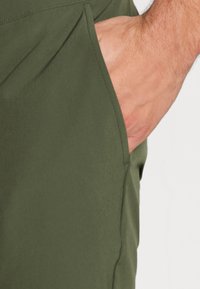 Pantalones cortos de tela verde con un bolsillo lateral, con una textura suave y un diseño minimalista. Las costuras acolchadas crean un aspecto estructurado.
