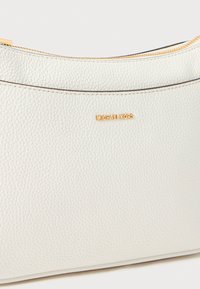 Balto žvyrinė oda pagaminta Michael Kors pakuotė su aukso spalvos užtrauktuku ir aukso logotipu, kuris yra centriškai uždėtas viršuje priekyje.